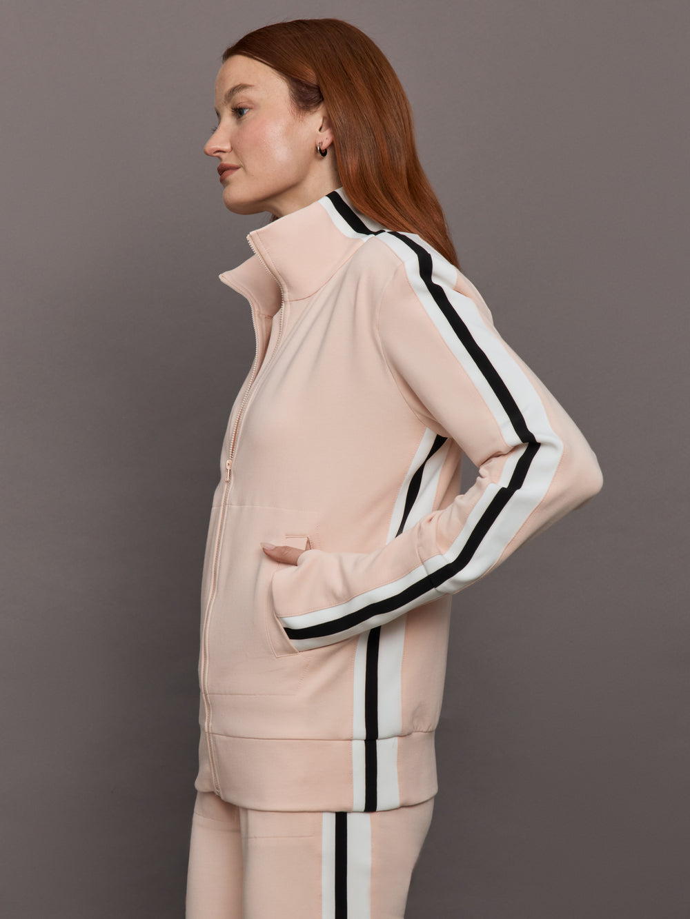 Model wears baby pink jacket with a turtleneck, front zipper, and side stripes on the sleeves.
