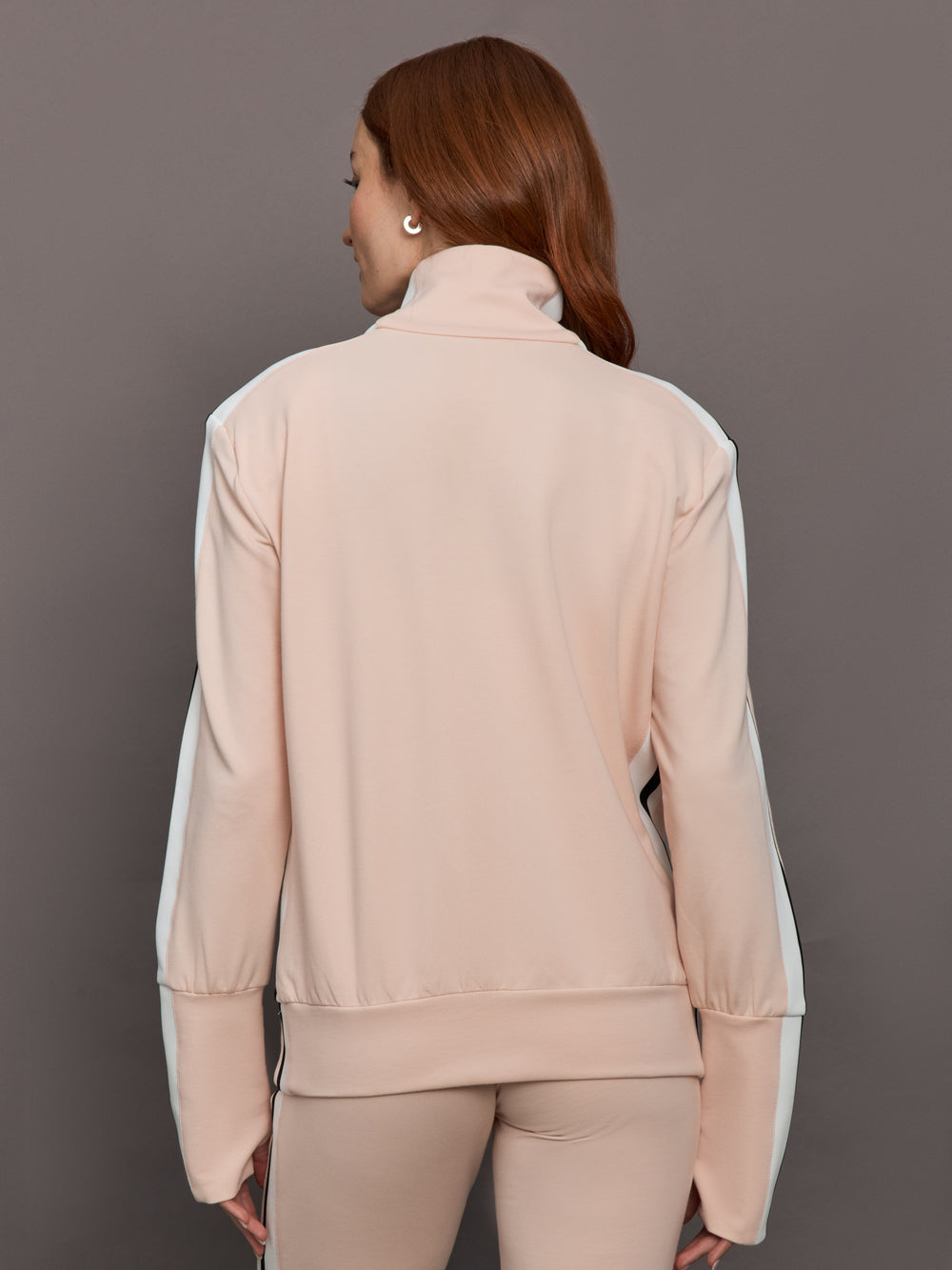 Model wears baby pink jacket with a turtleneck, front zipper, and side stripes on the sleeves.
