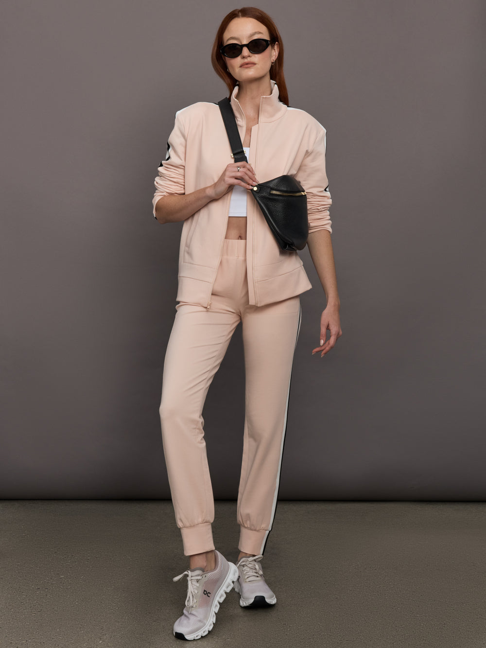 Model wears baby pink jacket with a turtleneck, front zipper, and side stripes on the sleeves.
