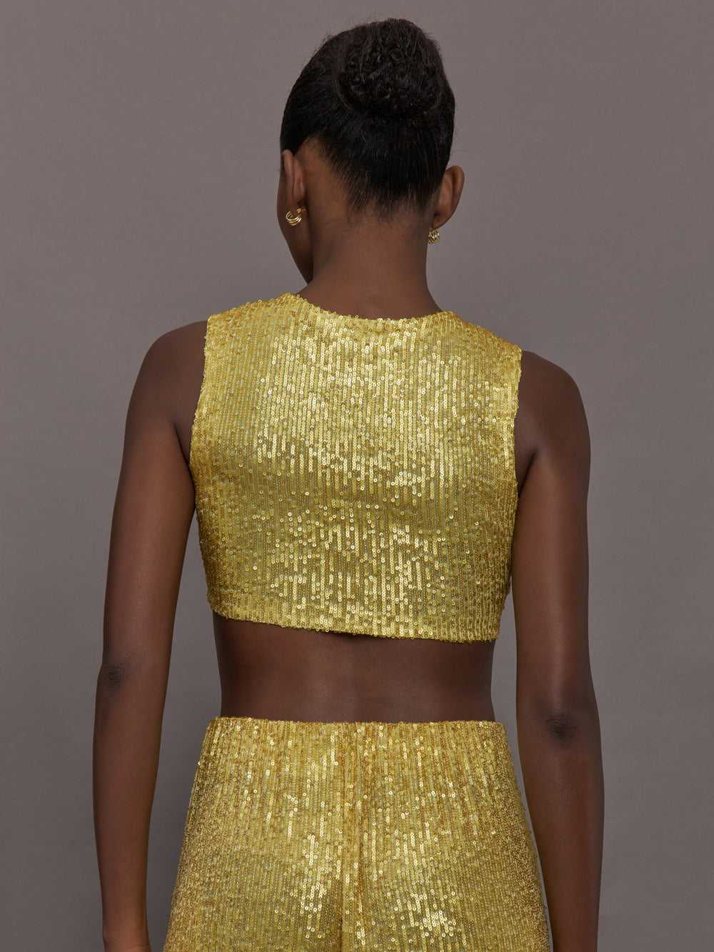 Model wears the Sleeveless Slim Fit Cropped Top in Asparagus, featuring a fitted, cropped, high neck design with sparkles.