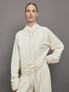 Model wears an oversized cream colored hoodie with extra long drawstrings. 
