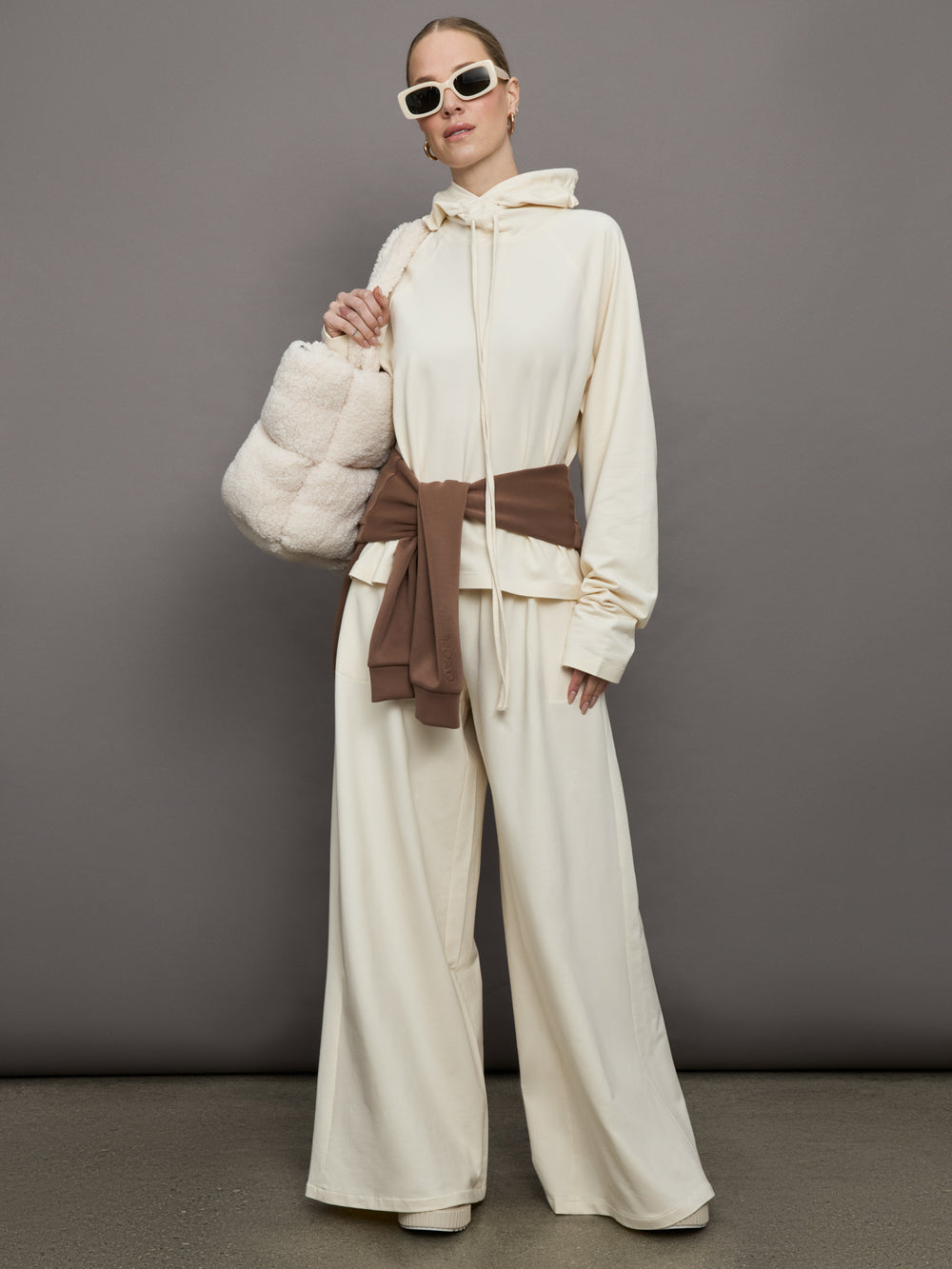 Model wears a pair of oversized wide leg cream colored sweatpants. 