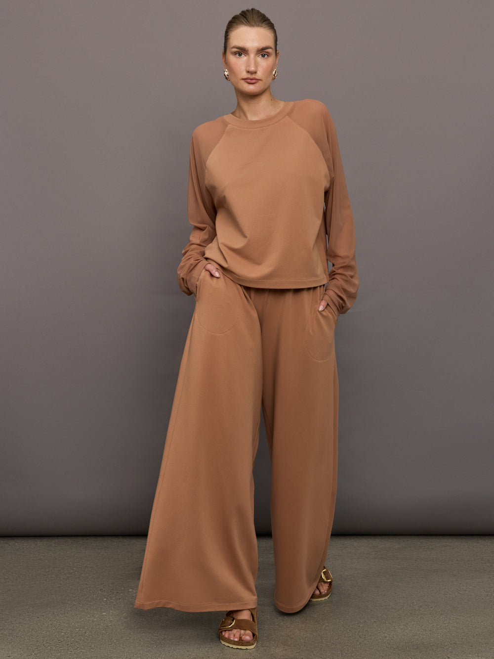 Model wears a pair of oversized, wide legged, light brown sweatpants.