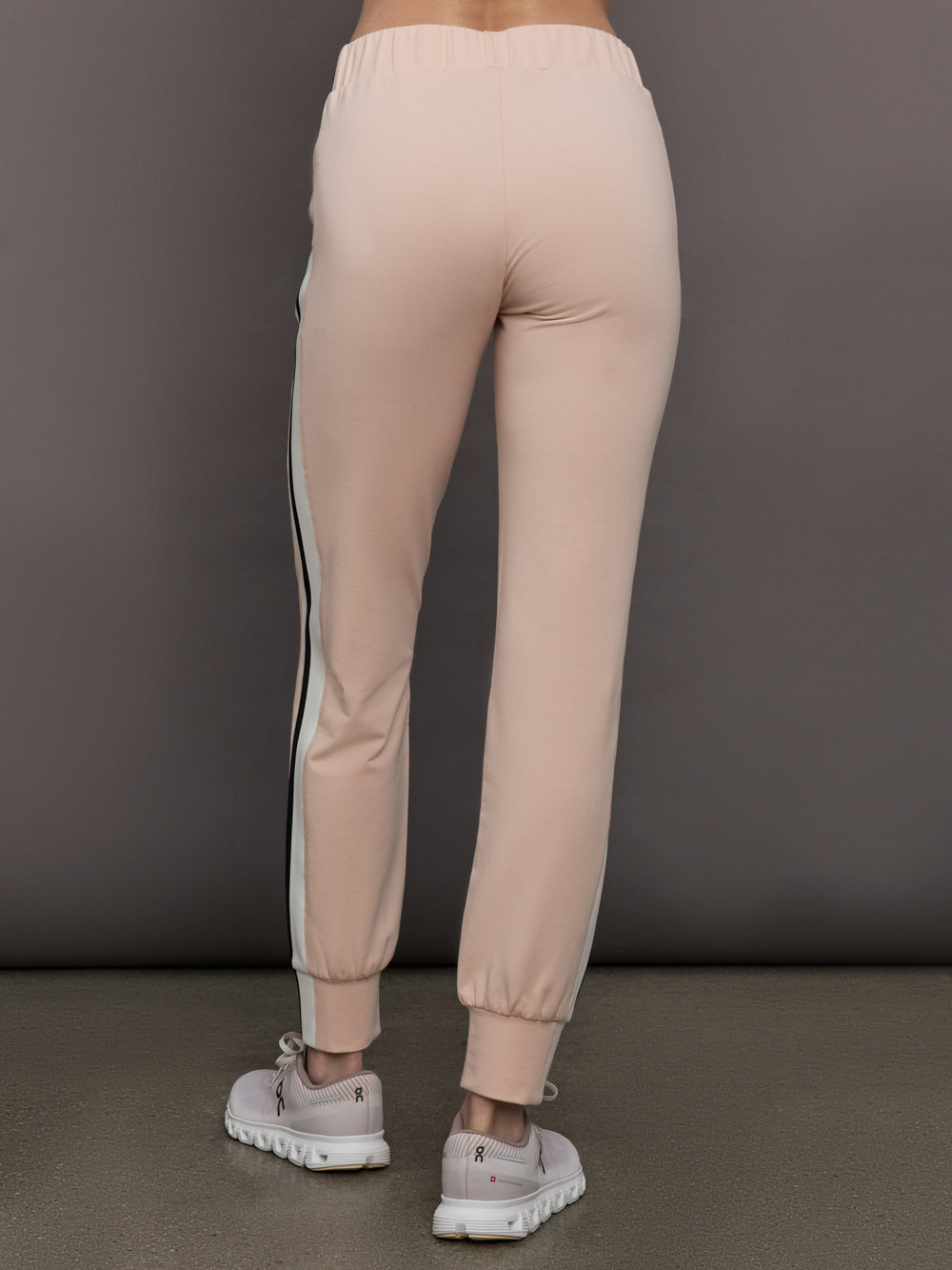 Model wears baby pink jogger pants with side stripes, elastic waistband, and cuffed ankles.
