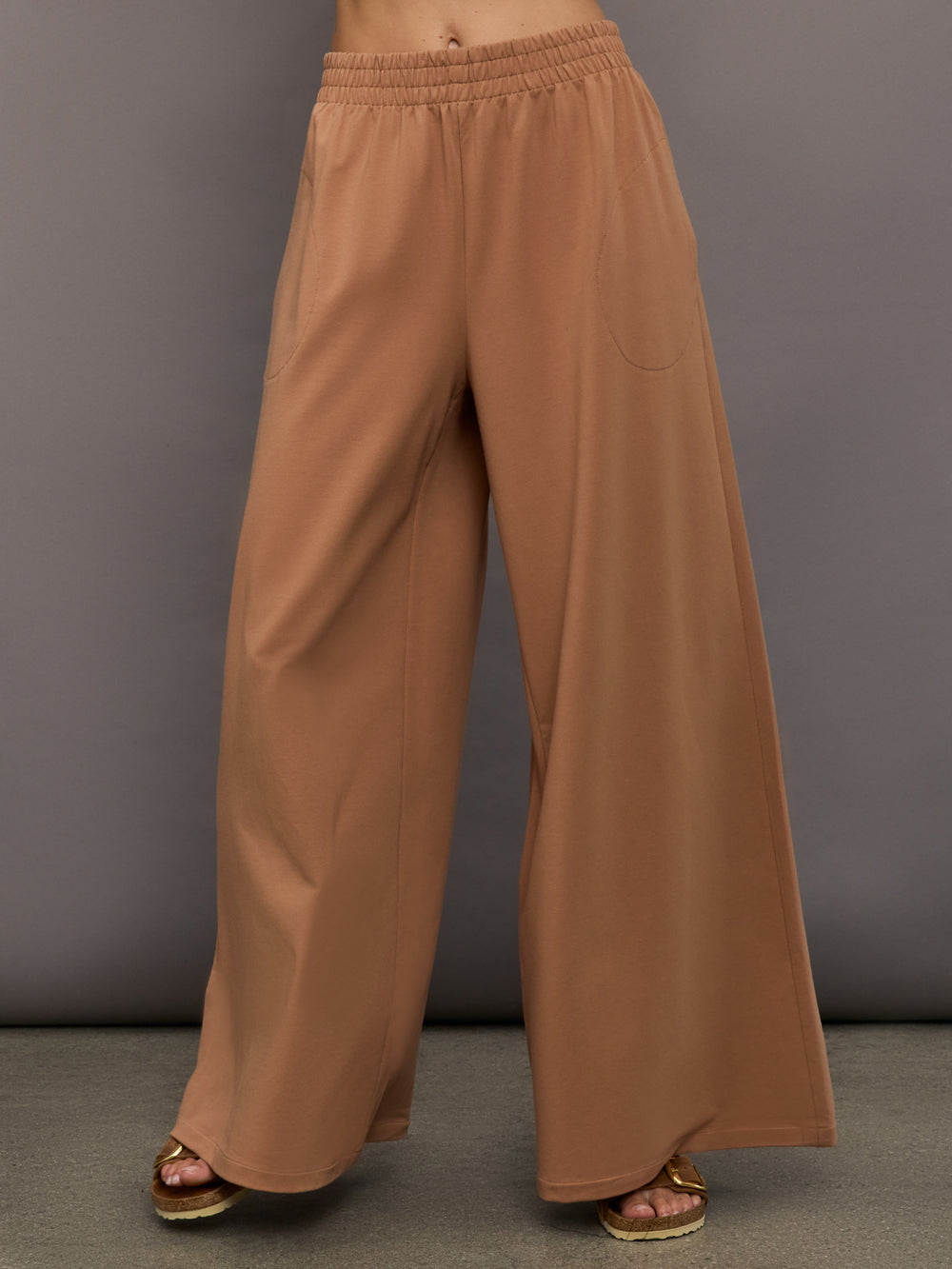 Model wears a pair of oversized, wide legged, light brown sweatpants.