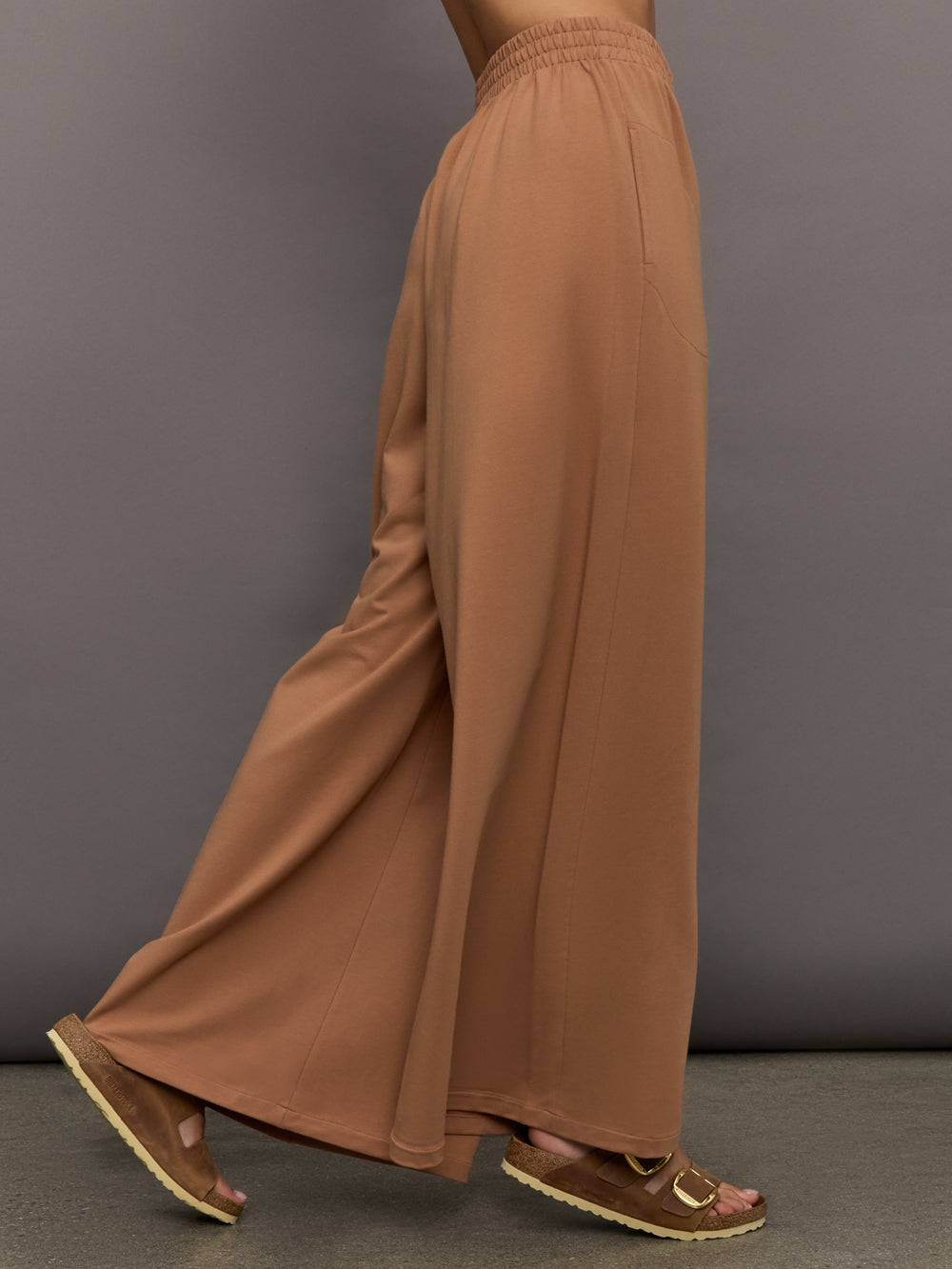 Model wears a pair of oversized, wide legged, light brown sweatpants.