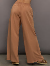 Model wears a pair of oversized, wide legged, light brown sweatpants.