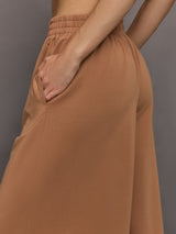 Model wears a pair of oversized, wide legged, light brown sweatpants.
