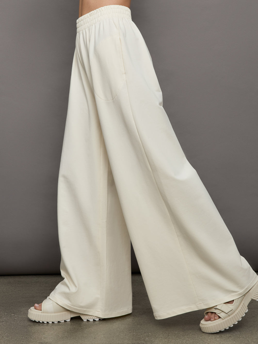Model wears a pair of oversized wide leg cream colored sweatpants. 