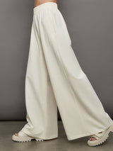 Model wears a pair of oversized wide leg cream colored sweatpants. 