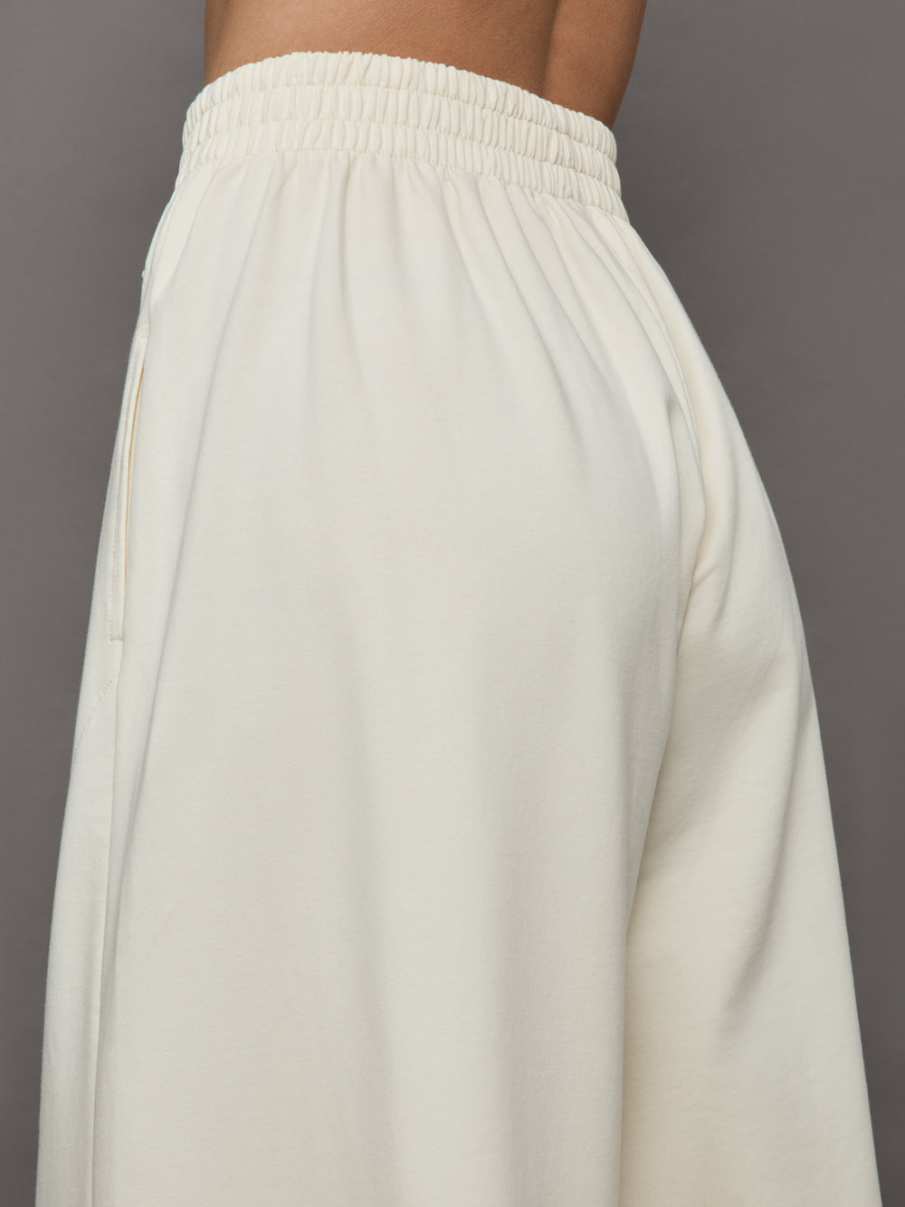 Model wears a pair of oversized wide leg cream colored sweatpants. 