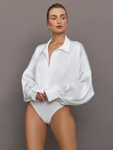 Model wears a white long sleeved bodysuit with oversized cuffed sleeves and a collar. 