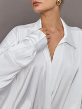 Model wears a white long sleeved bodysuit with oversized cuffed sleeves and a collar. 