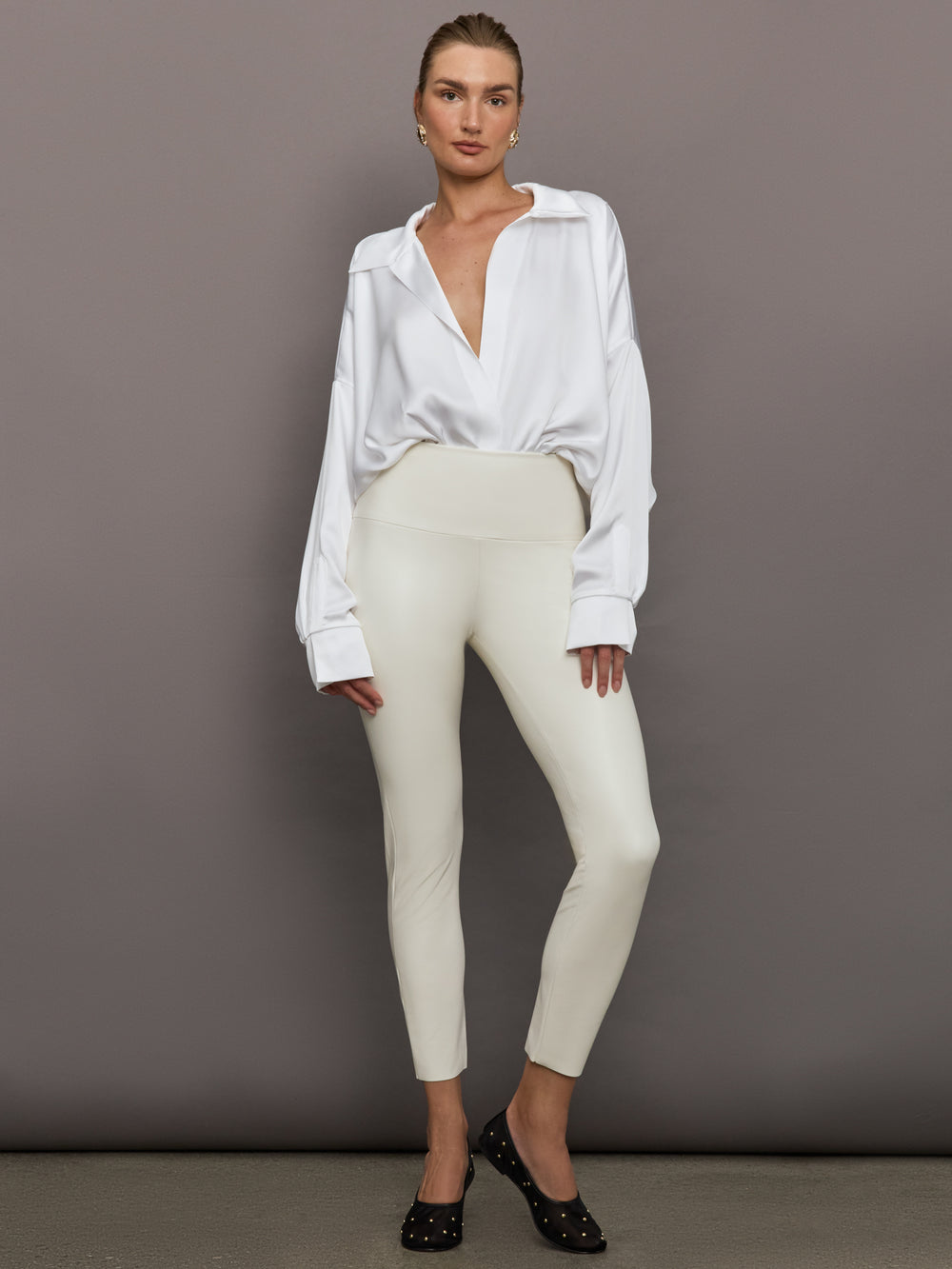 Model wears a white long sleeved bodysuit with oversized cuffed sleeves and a collar. 