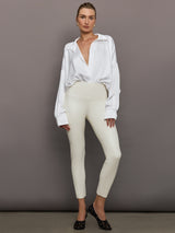 Model wears a white long sleeved bodysuit with oversized cuffed sleeves and a collar. 
