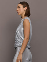 Model is wearing sleeveless twist top in silver, side view.