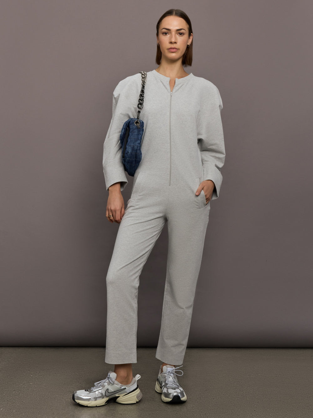 Model is wearing Bomber 1980s Zip Front Jumpsuit in Light Heather Grey, full body styling.