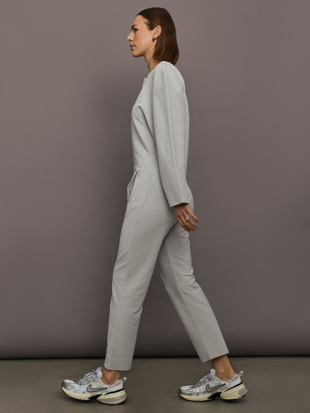 Model is wearing Bomber 1980s Zip Front Jumpsuit in Light Heather Grey, side profile view.