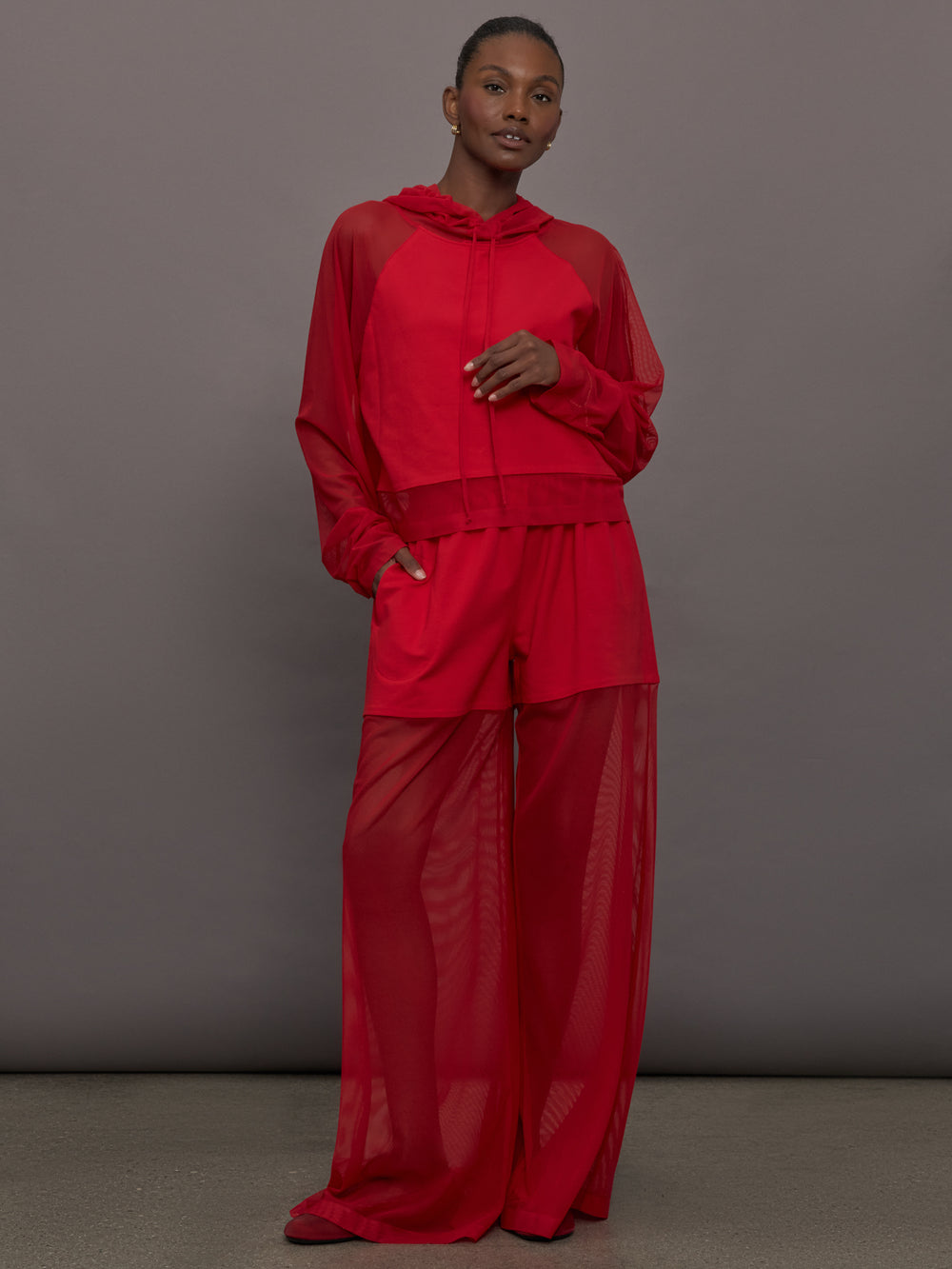 Model wears the Oversized Raglan Sleeve Hooded Cropped Top in Tiger Red, with mesh raglan sleeves and a mesh hood with a breathable design with a relaxed fit.