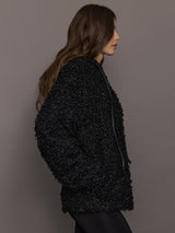 Woman wearing a textured black coat against a plain background