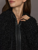 Close-up of a person wearing a black textured jacket with a zipper, on a neutral background.