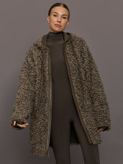 Woman wearing a long, textured coat against a gray background