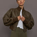 Person wearing a brown leather jacket over a white shirt on a gray background