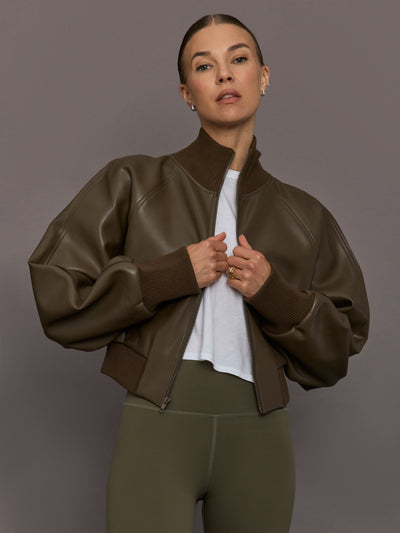 Person wearing a brown leather jacket over a white shirt on a gray background