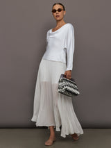Woman wearing a white top and sheer white skirt holding a black and white handbag against a gray background