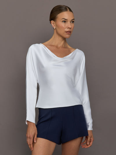 Woman wearing a white long-sleeve top and navy shorts against a gray background