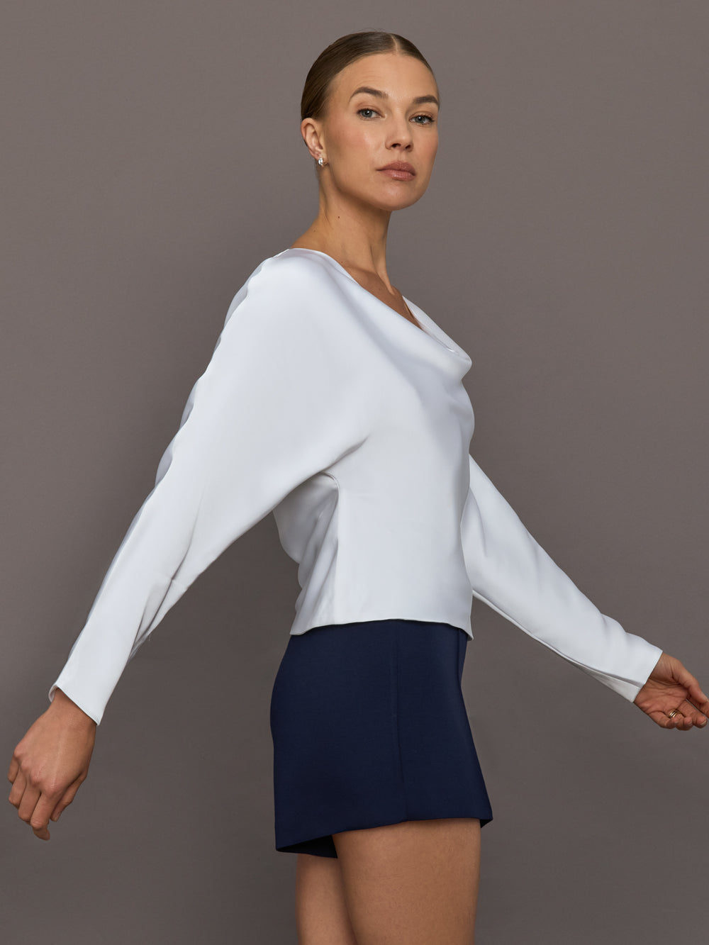 Woman wearing a white long-sleeve top and navy skirt against a gray background