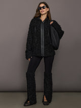 Woman wearing a black textured outfit with sunglasses against a gray background