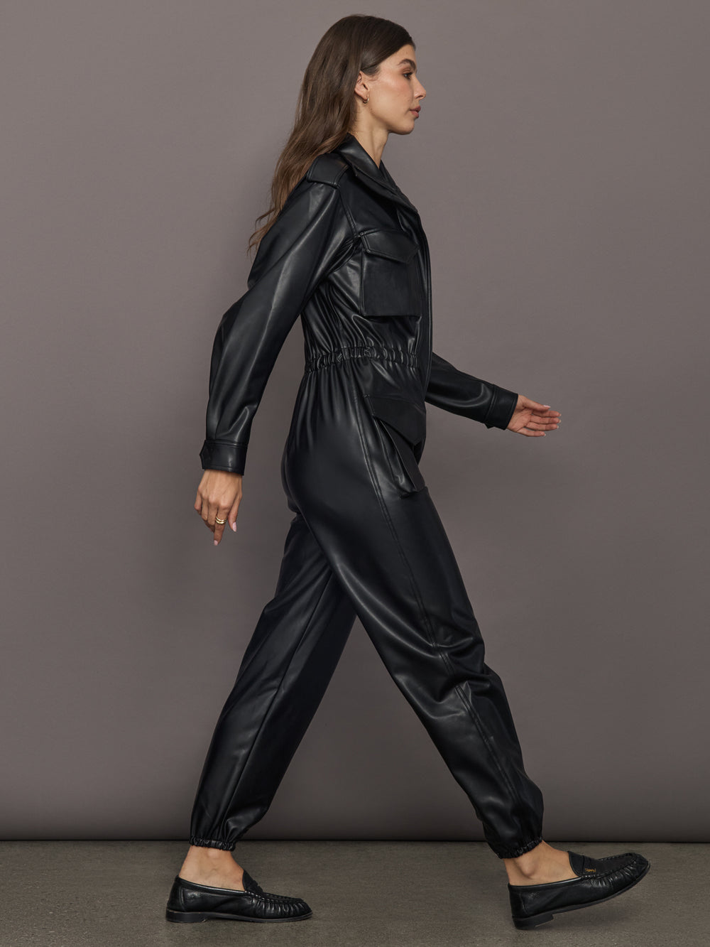 Woman wearing a black leather outfit walking against a gray background