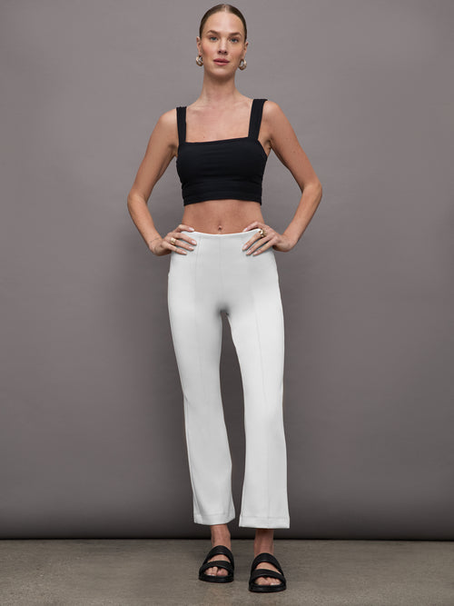 Model wearing cropped white flare pants styled with black crop top, full body view.