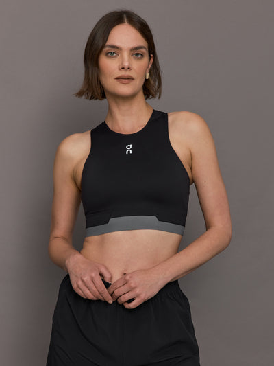 Model is wearing the Train 2-in-1 crop top in back with grey accents, and a tight, supportive fit, as well as a high neck.