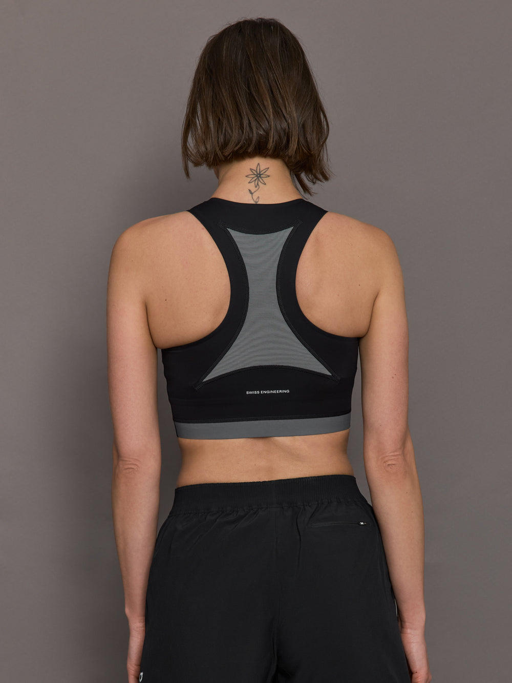 Model is wearing the Train 2-in-1 crop top in back with grey accents, and a tight, supportive fit, as well as a high neck.