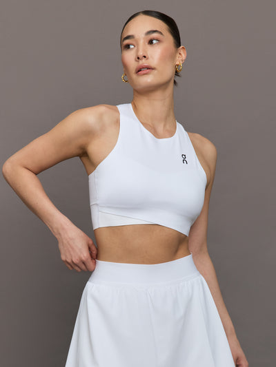 Model wears white cropped tank top with wide shoulder straps and a high neckline.