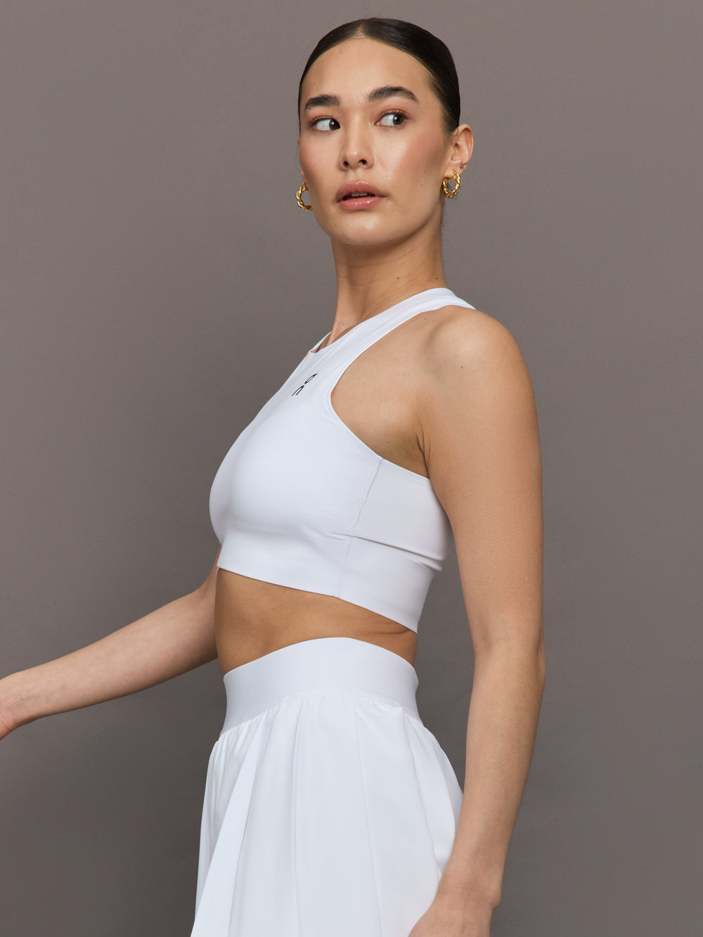 Model wears white cropped tank top with wide shoulder straps and a high neckline.