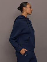 Model is wearing On Focus Tech Hoodie for women in navy with drawstring hood, kangaroo pocket, and relaxed silhouette, side view.