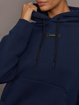 Close-up of On Focus Tech Hoodie for women in navy highlighting drawstring hood, logo detail, and kangaroo pocket.