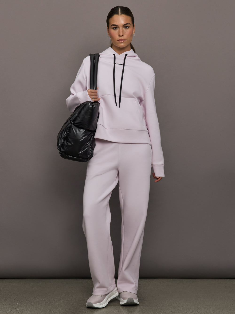 Person wearing a light gray tracksuit holding a black bag against a gray background