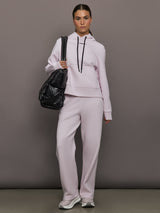 Person wearing a light gray tracksuit holding a black bag against a gray background