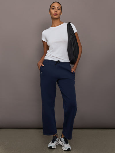Model is wearing On Focus Tech Sweatpants for women in navy styled with white t-shirt, sneakers, and black shoulder bag, full front view.