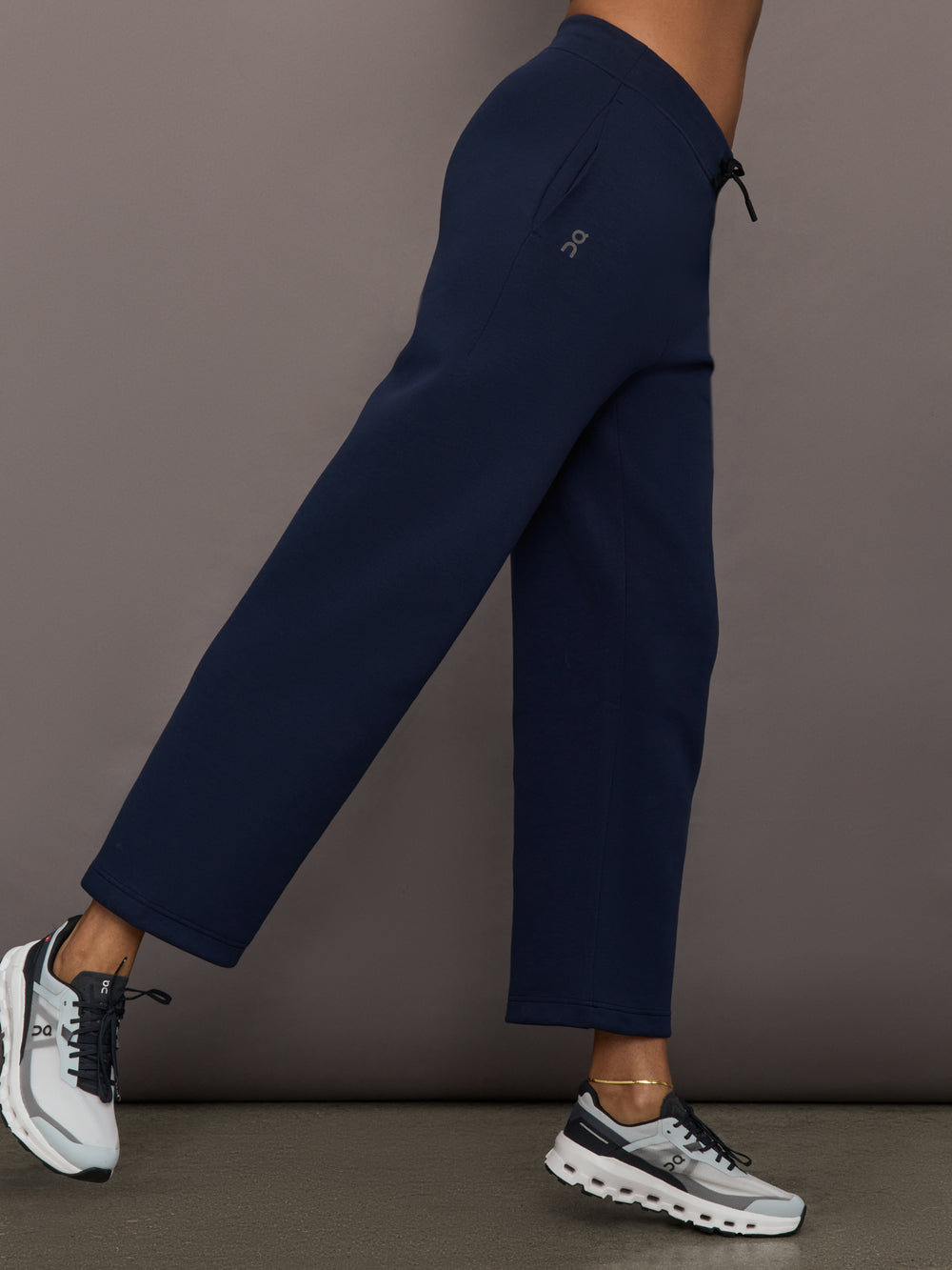 Model is wearing On Focus Tech Sweatpants for women in navy with relaxed straight leg and mid-rise drawstring waistband, side view.