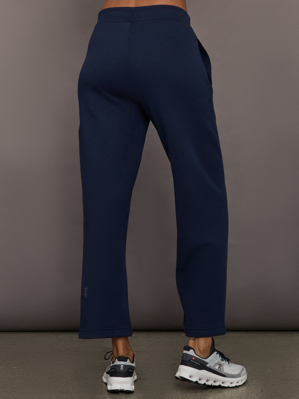Model is wearing On Focus Tech Sweatpants for women in navy with clean back design, straight leg fit, and ankle-length cut, back view.