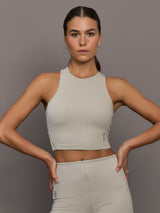 Model wears a high neck sleeveless cropped top in light sandy brown. 