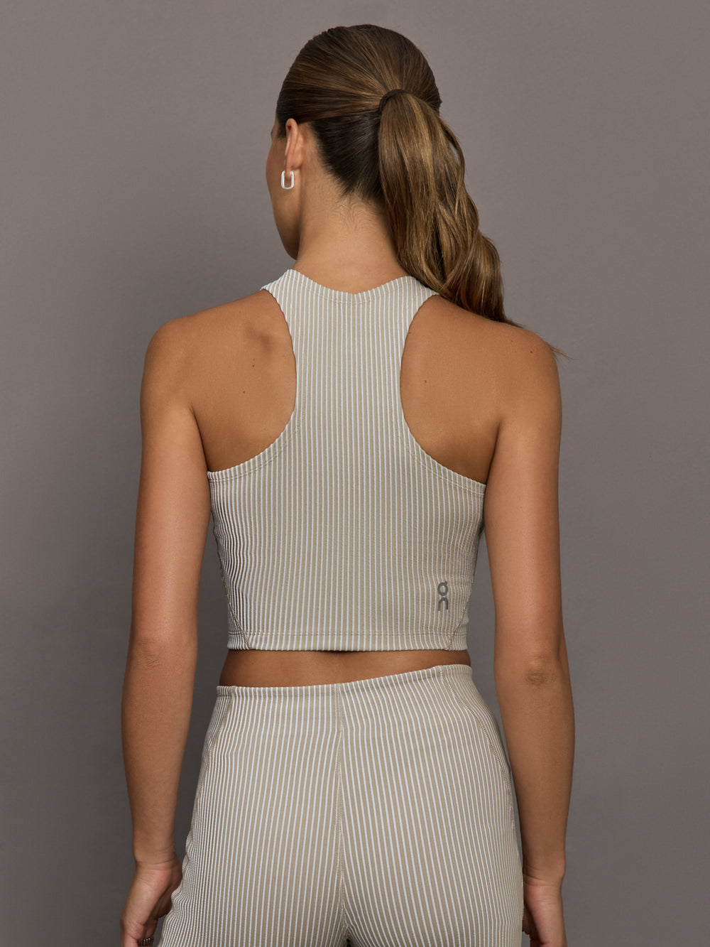 Model wears a high neck sleeveless cropped top in light sandy brown. 