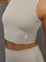 Model wears a high neck sleeveless cropped top in light sandy brown. 