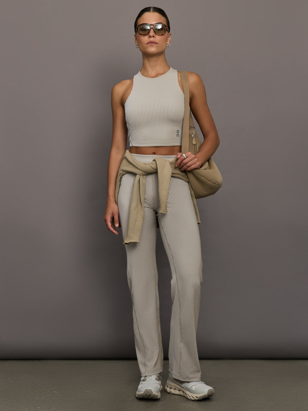 Model wears a high neck sleeveless cropped top in light sandy brown. 