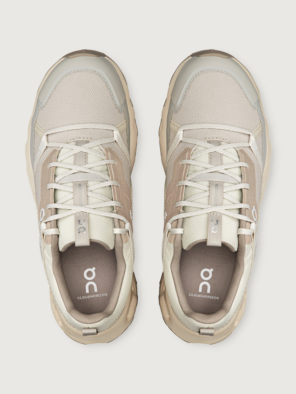Pair of beige sneakers with white laces on a light gray background